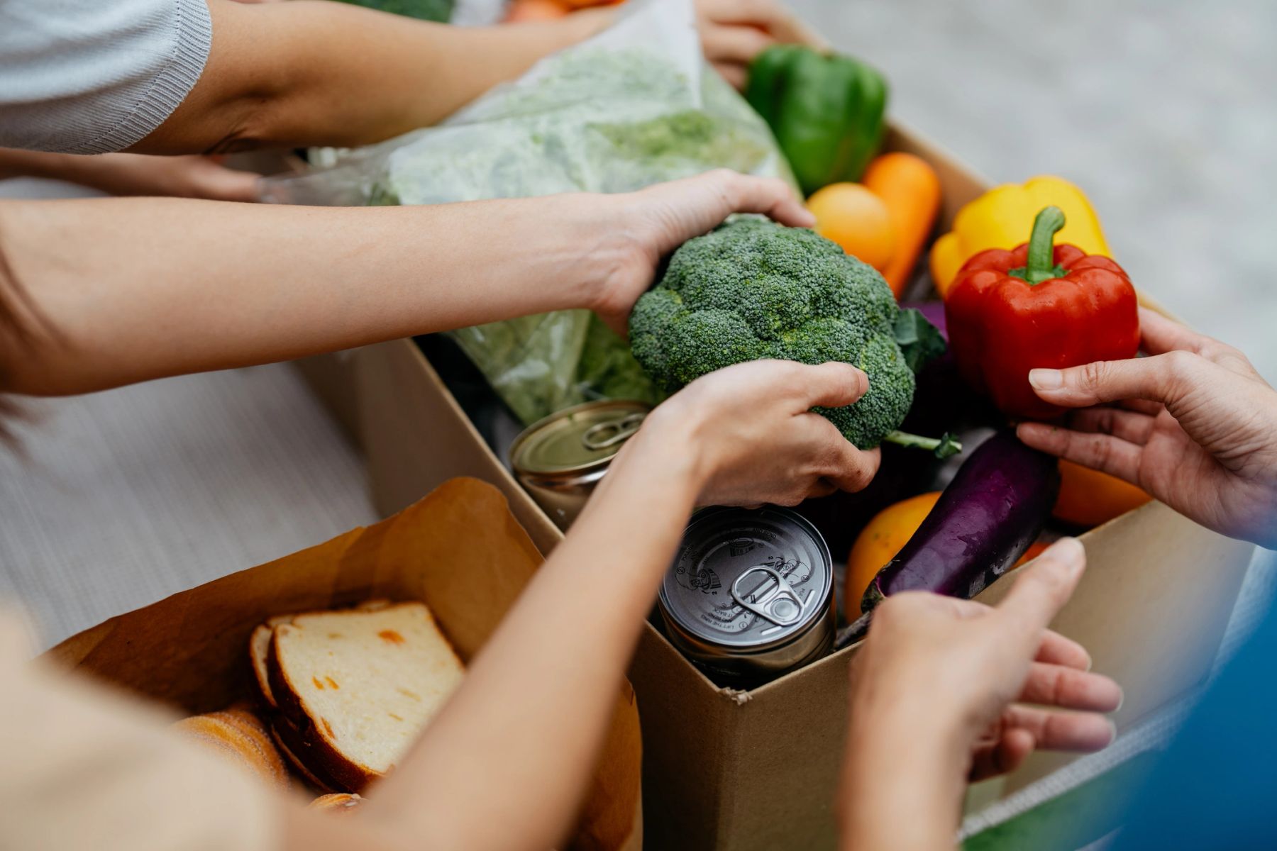 People exchanging fresh groceries including broccoli and bell pepper.